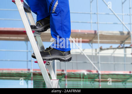 Close-up Of A Handy Repair Man Standing On Steel Ladder Against Construction Sites Stock Photo