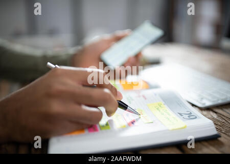 Close-up Of Businessman Writing Schedule In Calendar Diary On Desk Stock Photo