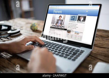 Close-up Of Businessperson Checking Online News On Laptop At Desk Stock Photo