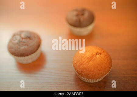 Two chocolate muffins and one creamy on the brown wooden table. Stock Photo