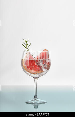 A glass of gin and tonic with slices of grapefruit, green rosemary, ice cubes and fizz Stock Photo