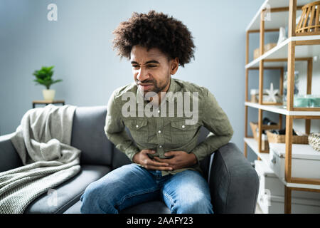 Midsection Of Man With Stomach Ache Sitting On Couch At Home Stock Photo