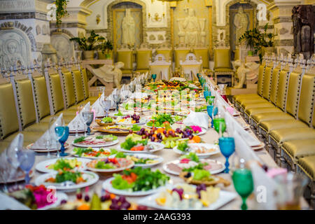 Beautifully served table for a banquet in a restaurant. White napkins and blue and green wine glasses on the table. A number of old chairs Stock Photo