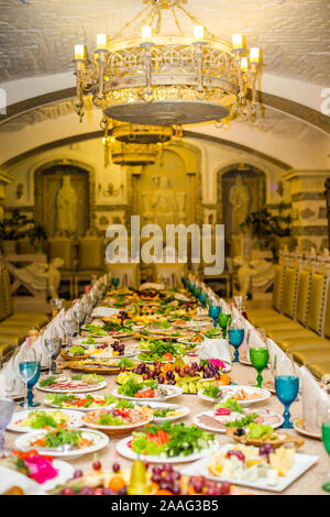 Beautifully served table for a banquet in a restaurant. White napkins and blue and green wine glasses on the table. A number of old chairs Stock Photo
