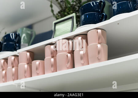Mugs on shelf on a shelf in retail gift store. Pink and dark blue coffee mugs on shelf in kitchen. Stack of ceramic cups on shelf, stack of clean cera Stock Photo