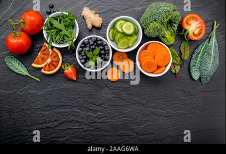 Colourful healthy smoothies and juices in bottles with fresh tropical fruit and superfoods on dark stone background with copy space. Stock Photo