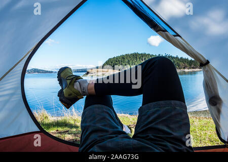 A first person point of view of a man's legs crossed in the entrance to a tent on Skagit Island, Washington, USA. Stock Photo