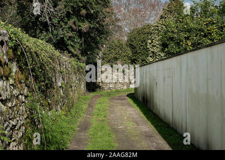 narrow way sided by one old stonewall and white concrete wall. Stock Photo
