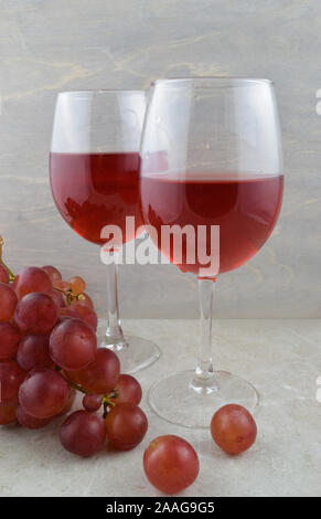Two glasses of luxe red wine paired with fresh red grapes on a gray stone background. Stock Photo
