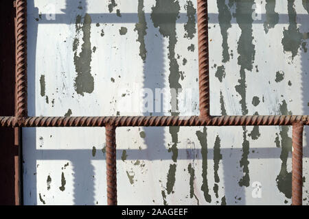 Fragment of an old window painted by white paint behind a rusty brown bars on a sunny day. Abstract background Stock Photo