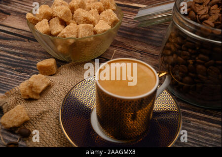 A Cup of coffee, pieces of brown sugar in a sugar bowl, coffee beans in a glass jar on a wooden background Stock Photo