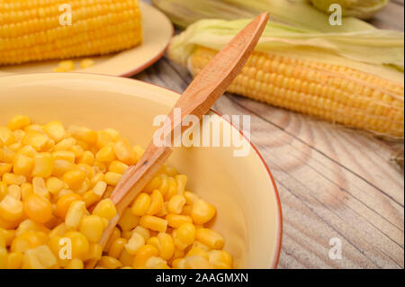 Grains of sweet corn in a plate with a wooden spoon and ears of corn on the table. Healthy diet. Fitness diet. For a sweet treat. Close up Stock Photo