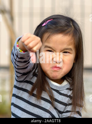 Portrait of angry frustrated little girl throwing a thumb down gesture at the camera with a furious vengeful expression outdoors Stock Photo