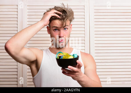 Man with unshaven face holds bowl with measuring tape. Guy with surprised face expression on background of beige jalousie. Fitness lifestyle idea. Weight management and sportive diet concept Stock Photo