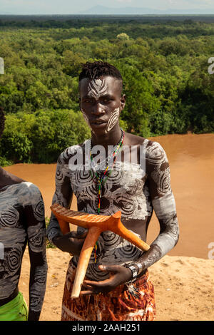 Ethiopia, South Omo, Kolcho Village traditionally dressed young Karo tribe man above Omo River holding hand made wooden stools to sell to tourists Stock Photo