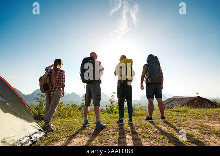 Group of four young hikers stands near tent and looks at sunrise and islands Stock Photo
