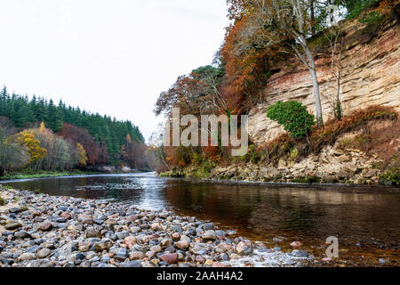 RIVER IN EARLY WINTER AUTUMNAL LEAVES ON THE TREES AND SHINING STONES AND PEBBLES ON THE RIVER BANK Stock Photo