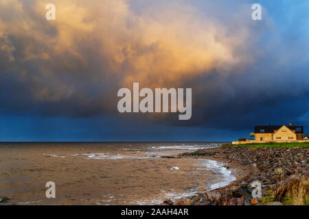 SUNSET AND A HEAVY RAIN CLOUD OVER THE SHORELINE A HOUSE AND THE SEA Stock Photo