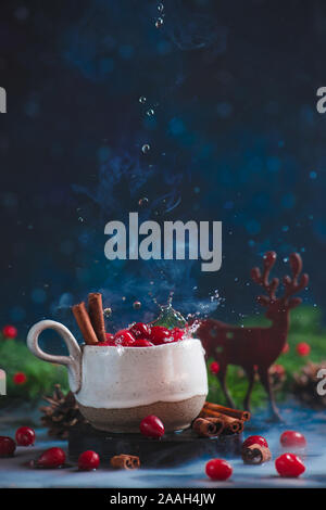 Cranberry winter drink with water drops, cinnamon, steam, and a wooden decorative deer. Stock Photo