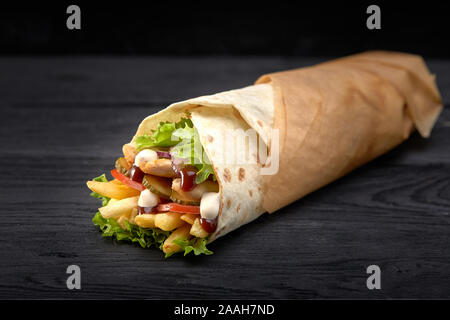 Tasty doner kebabs with fresh salad trimmings and shaved roasted meat served in tortilla wraps on brown paper as a takeaway snack. Stock Photo