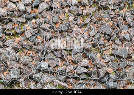 Gravel covered with metal wire is on the ground, background photo texture, top view. Landslide protection made of crushed stones under metal grid Stock Photo