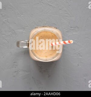 Homemade smoothie with coffee, oat and banana in a glass jar mug on a gray surface, top view. Overhead, from above. Stock Photo
