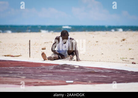 A lone man on the shore of Lake Malawi mends his fishing net Stock Photo