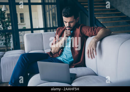 Portrait of serious focused guy working on his laptop read information think want choose decide right job solution decision choice review sit divan in Stock Photo