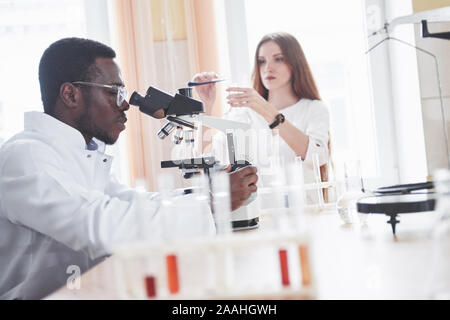 The scientist works with a microscope in a laboratory conducting experiments and formulas. Stock Photo
