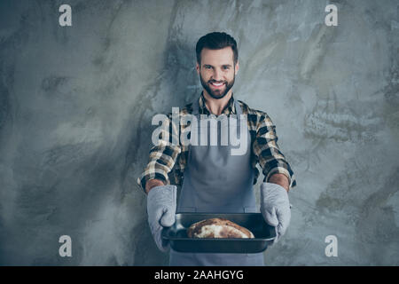 Photo of cheerful positive cook chef having cooked his branded bread serving this to you in gloves isolated wall concrete grey color background Stock Photo