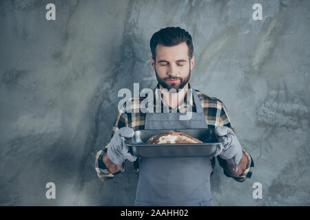 Photo of smiling cheerful positive handsome cook having baked bread and smelling its fantastic flavor in tray isolated grey color wall concrete Stock Photo