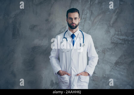 Portrait of serious talented doctor put his hands in pockets of white coat look ready to cure patients in clinic isolated over grey color background Stock Photo