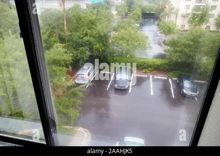 looking out of an upper floor hotel room in heavy rain thunderstorm down onto flooding parking lot in jacksonville florida usa Stock Photo