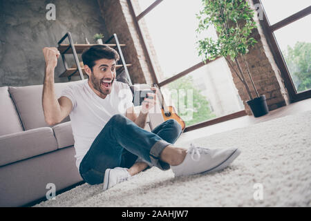 Hooray. Photo of mixed race crazy guy sitting floor leaning sofa holding telephone reading unexpected positive news blog subscribers wear casual Stock Photo