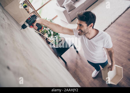 High angle view photo of mixed race arabian guy installing new wall shelf using drill manual repair of new flat happy craftsman working with pleasure Stock Photo