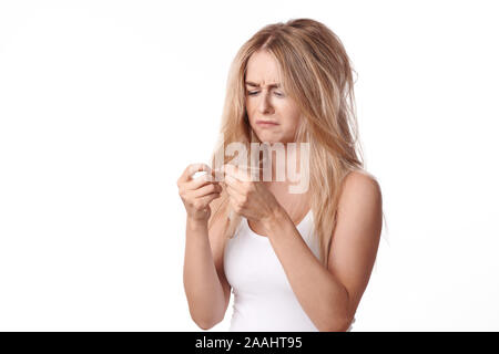 Pretty young woman having a bad hair day standing looking dejectedly at the dry ends of her tousled long blond hair as she holds them up in her hands Stock Photo