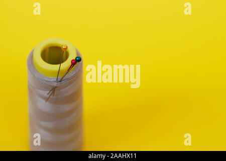 Needlework concept. One large spool of thread and needle on a yellow background. Plenty of room for text. Skein of thread for needlework and sewing. Stock Photo