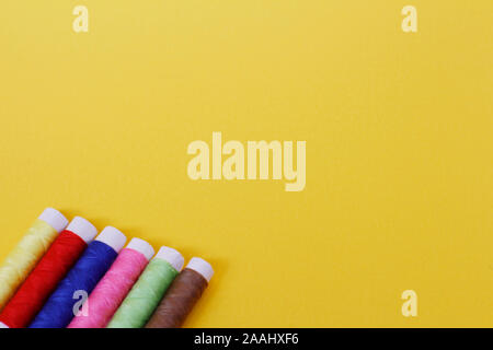 Needlework concept. A lot of multi-colored little bobbins of sewing thread on a yellow background. Plenty of room for text. Skeins of thread for needl Stock Photo