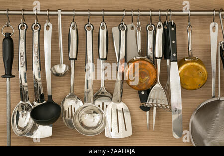 Batterie de cuisine, kitchen spoons, ladles, copper saucepans, fish slices, knife sharpening steel and kitchen utensils hanging on a wall bracket Stock Photo