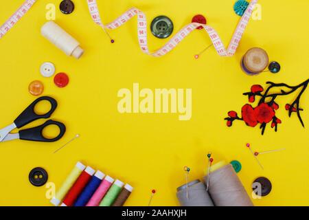 Sewing buttons and threads on a yellow background. Needlework concept. A lot of multi-colored little bobbins of sewing thread on a yellow background. Stock Photo