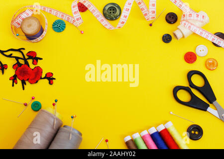 Sewing buttons and threads on a yellow background. Needlework concept. A lot of multi-colored little bobbins of sewing thread on a yellow background. Stock Photo