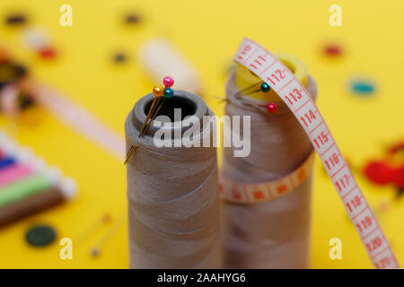 Sewing buttons and threads on a yellow background. Needlework concept. A lot of multi-colored little bobbins of sewing thread on a yellow background. Stock Photo