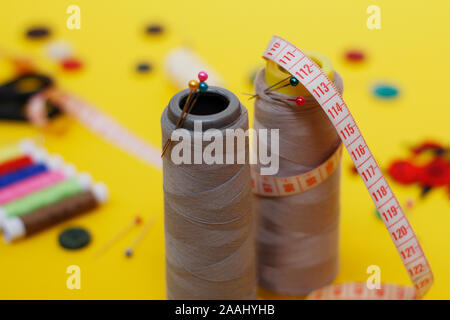 Sewing buttons and threads on a yellow background. Needlework concept. A lot of multi-colored little bobbins of sewing thread on a yellow background. Stock Photo