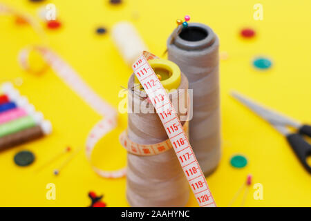 Sewing buttons and threads on a yellow background. Needlework concept. A lot of multi-colored little bobbins of sewing thread on a yellow background. Stock Photo