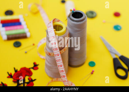 Sewing buttons and threads on a yellow background. Needlework concept. A lot of multi-colored little bobbins of sewing thread on a yellow background. Stock Photo