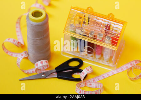 Sewing buttons and threads on a yellow background. Needlework concept. A lot of multi-colored little bobbins of sewing thread on a yellow background. Stock Photo