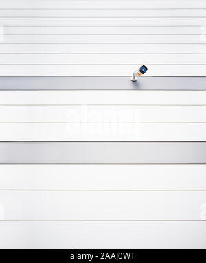 A surveillance CCTV camera on a wall of a modern white textured building Stock Photo