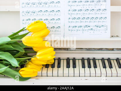 yellow tulips on a white piano with notes Stock Photo