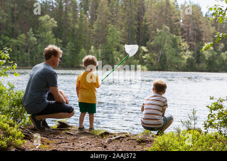 Father and sons playing with fish net by lake, Finland Stock Photo