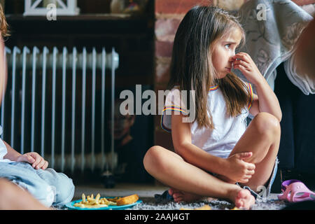 Girl sitting on rug beside radiator scratching nose Stock Photo